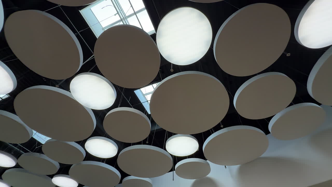 Round installations and lamps on the ceiling of the room. Low angle view. Windows on the ceiling at backdrop