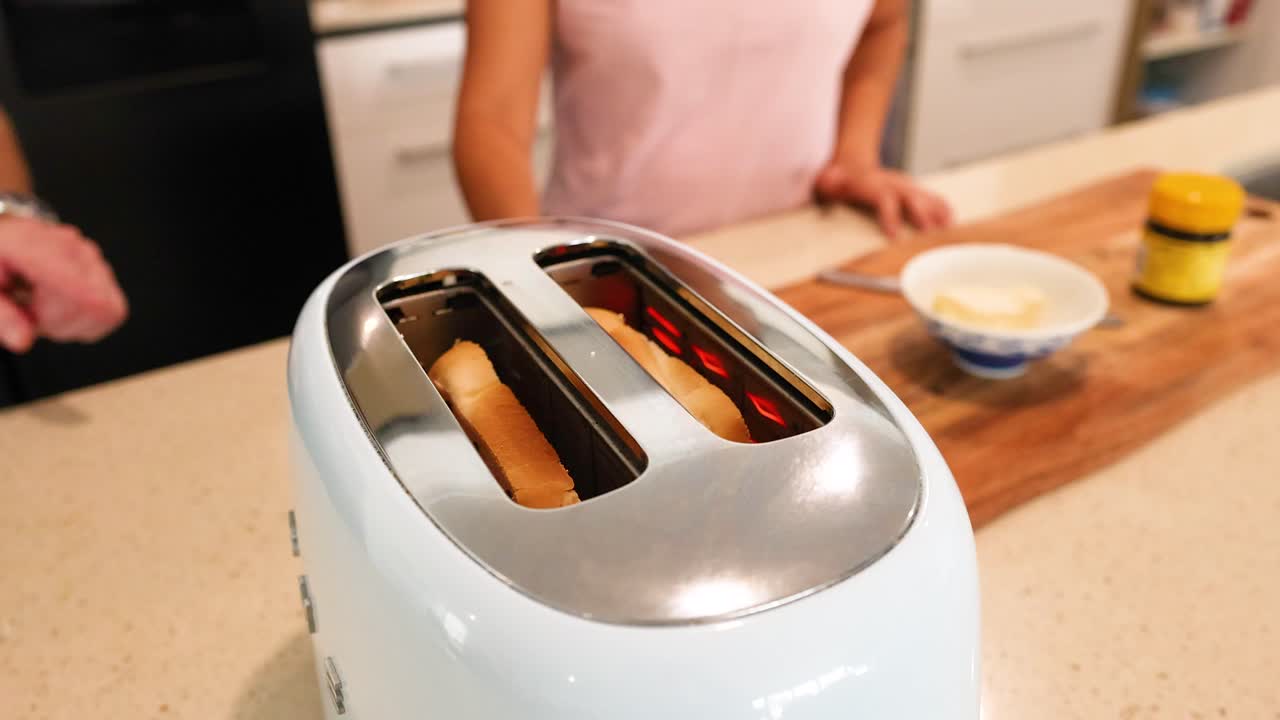 A toaster browns slices of bread in a bright kitchen, with a person nearby and breakfast items on the counter