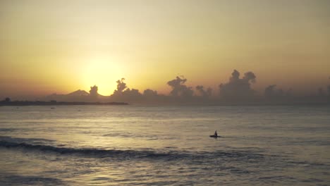 One-fisherman-on-a-boat-sailing-towards-the-sea-at-sunset-or-sunrise-with-dramatic-clouds-in-Bali,-Indonesia,-minimalism