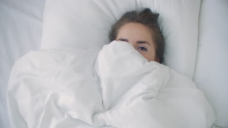 woman peeking under duvet and smiling.