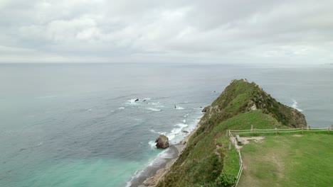 Fast-aerial-shot-passing-between-a-tree-and-Ermita-de-la-Regalina,-a-small-church-on-top-of-a-cliff-on-the-coast-of-Asturias,-Spain