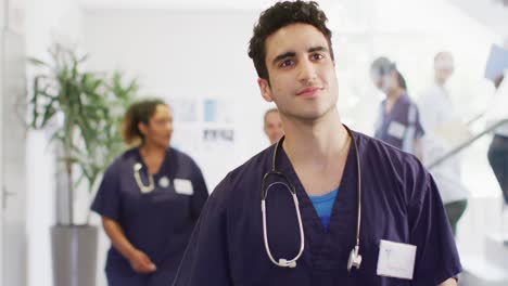 Video-of-smiling-biracial-male-doctor-walking-in-busy-hospital-corridor,-with-copy-space