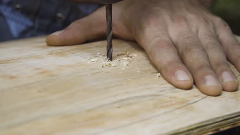 crafstman drilling hole in wooden plank for skateboard wheels to attach, close motion view