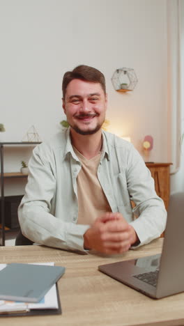 happy caucasian man freelancer waves hands hi gesture greeting at camera sitting at home office desk