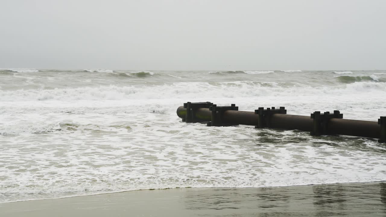 Rough ocean waves hitting pipeline on beach on a gloomy day in OCNJ