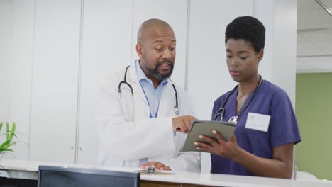 Médicos-Afroamericanos,-Hombres-Y-Mujeres,-Usando-Tabletas,-Hablando-En-El-Hospital