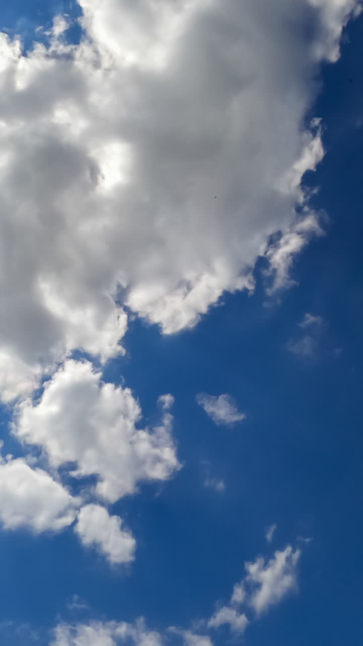 Bright sun shining in blue sky. Quickly flying white clouds against the sun. View from below. Timelapse. Vertical video