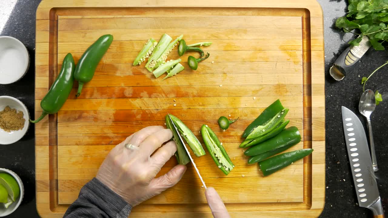 Overhead shot of slicing jalapeño chili peppers on a wood cutting board