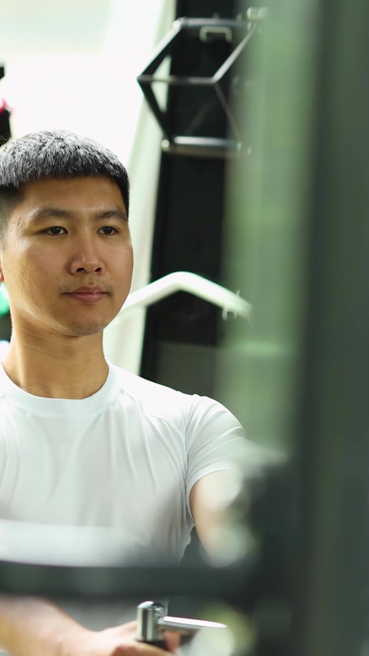 Uomo asiatico in maglietta bianca esegue un rematore con cavo da seduto in una palestra luminosa e moderna.