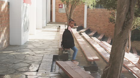 sitting on bench, african american girl with backpack waiting outside school building