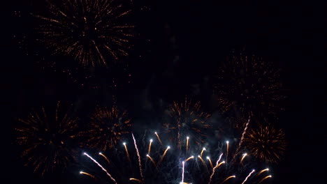 Fireworks-of-green,-purple,-and-gold-explode-in-the-night-sky