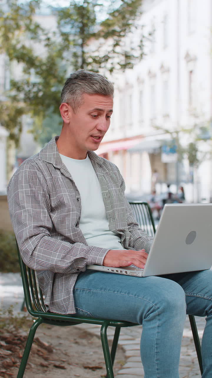 hombre maduro sentado en la calle de la ciudad mirando la cámara del portátil haciendo videoconferencia por cámara web
