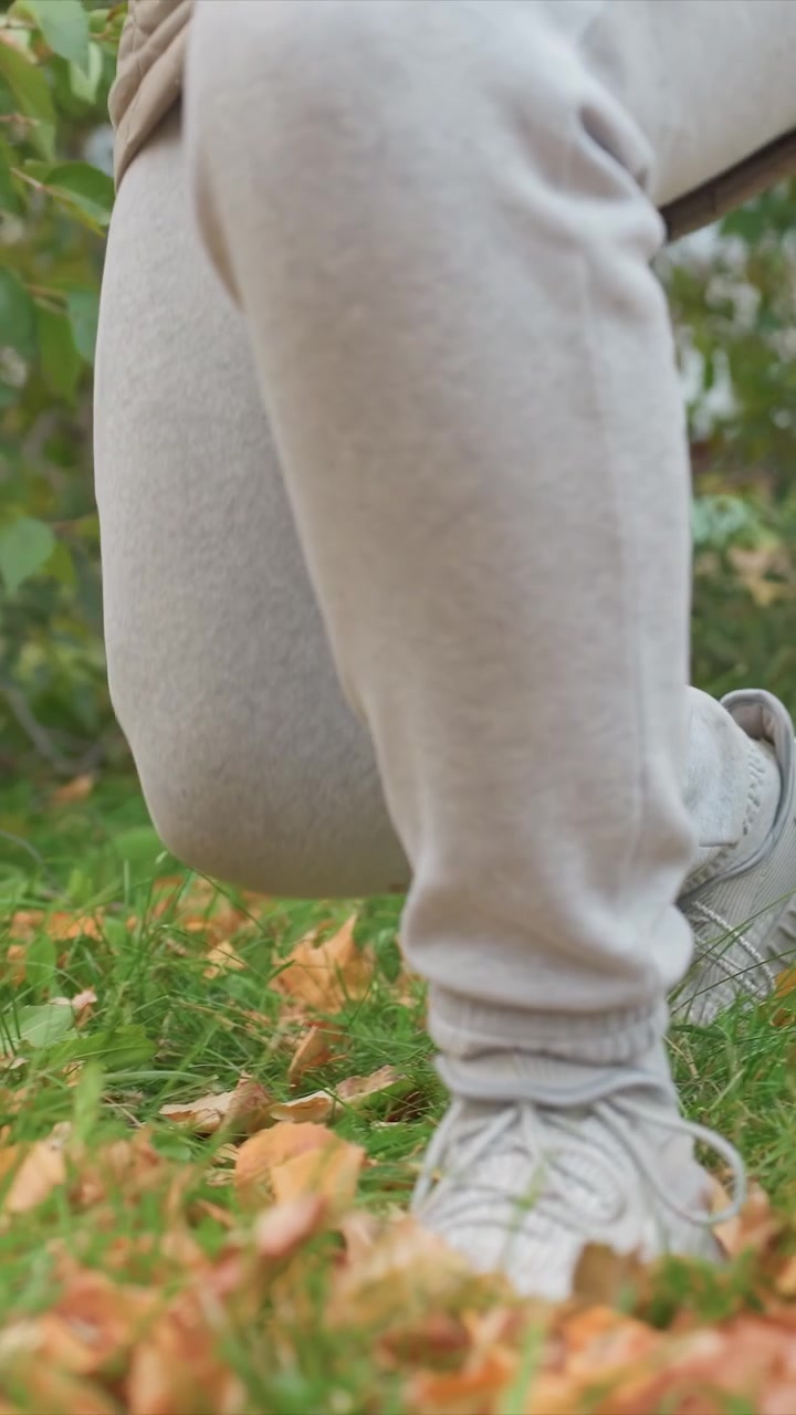 Person donning light gray bottoms stands amidst grasses. Body posture changes gently indicating slight activity. Environment shows open space filled with green vegetation