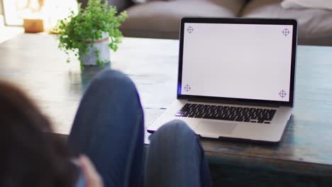 mujer biracial usando una computadora portátil con espacio de copia en la pantalla en casa
