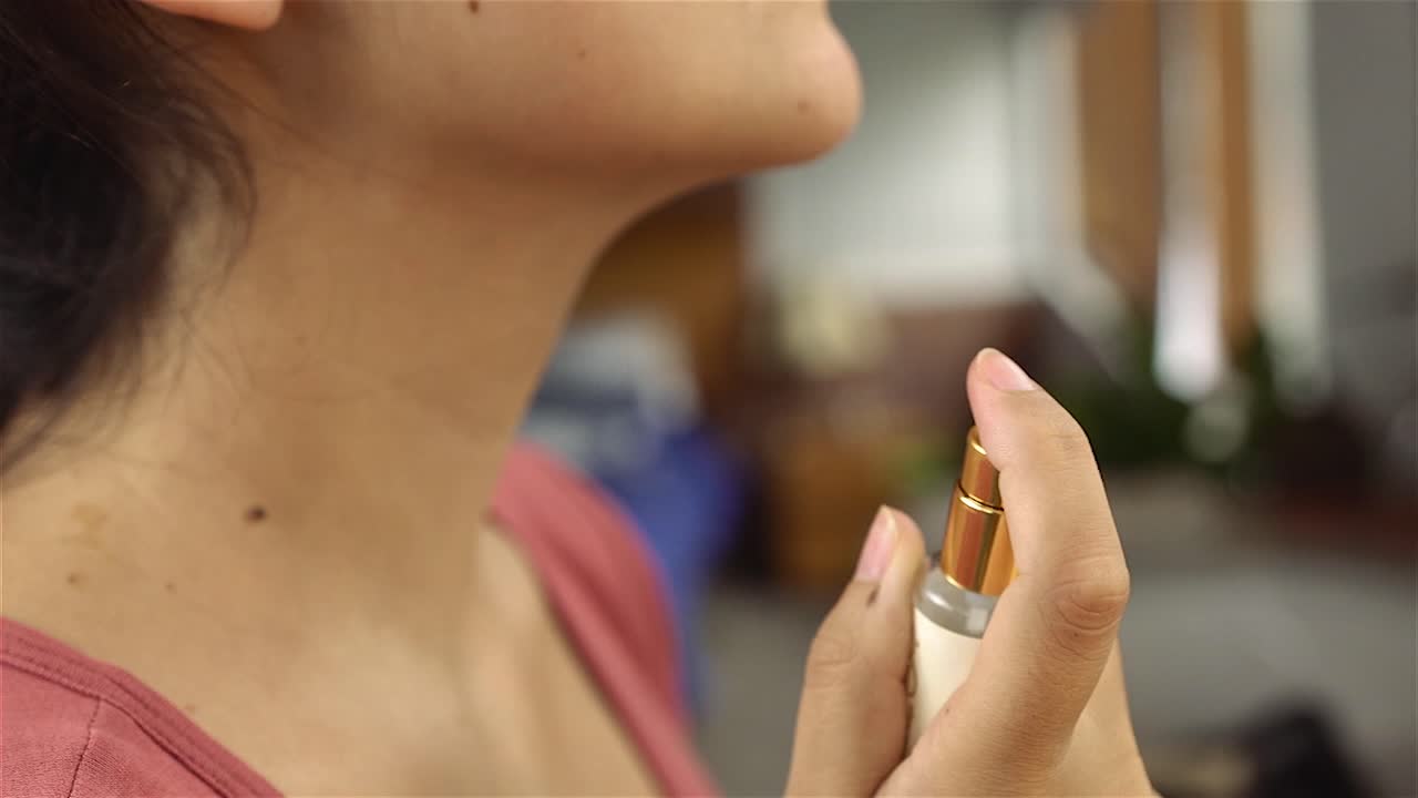 Bella giovane donna che spruzza delicatamente profumo sul collo in bagno.