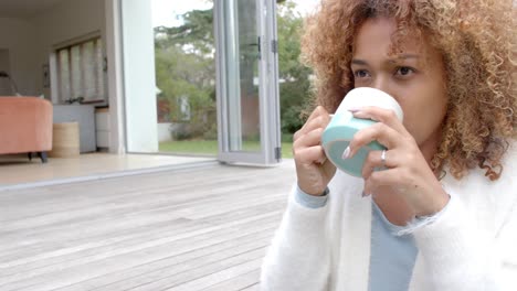 portrait of happy african american woman sitting on stairs and holding mug in garden, slow motion