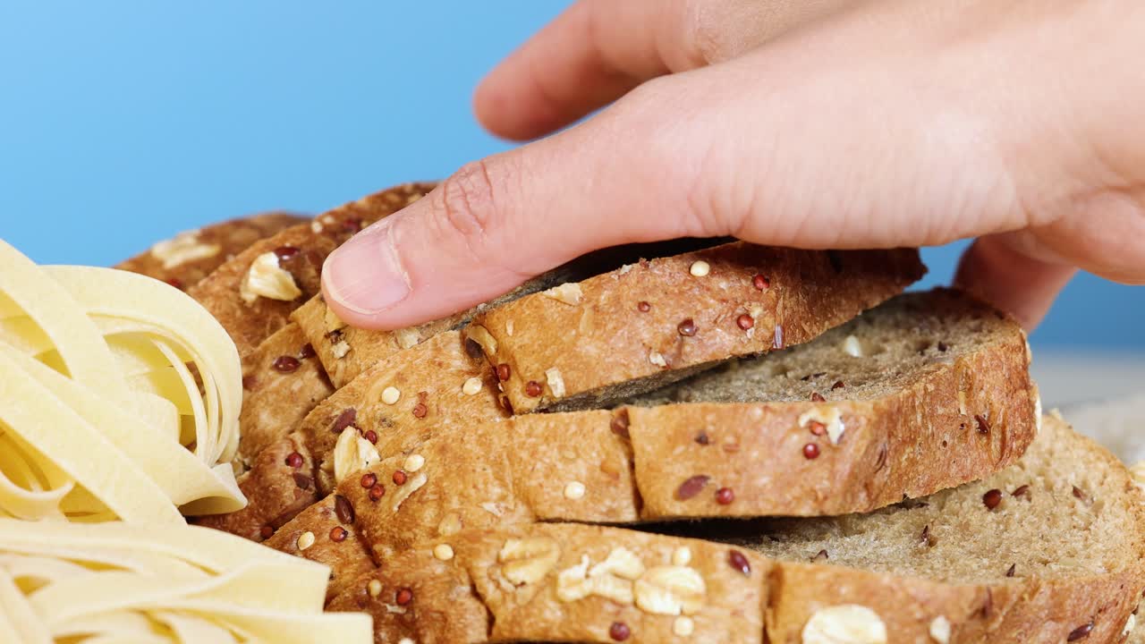 Hand reaching for a slice of whole grain bread next to pasta