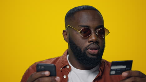 Closeup-bearded-afro-guy-using-credit-card-for-online-payment-in-studio.