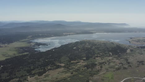 High-altitude-drone-shot-of-lake-surrounded-by-fields-and-forest