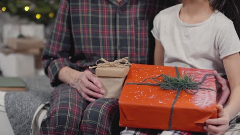 happy grandmother talking to her granddaughter while they are holding their gifts and looking at camera in christmas morning