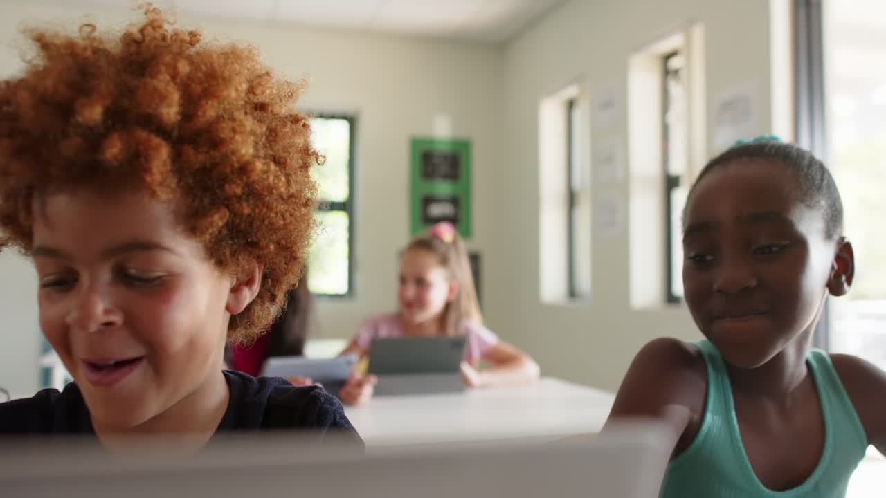 Camera shifting focus, boy and African American girl smiling then using tablet for class at school
