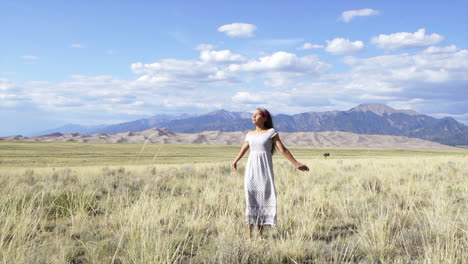 las grandes dunas de arena parque nacional de colorado a finales del verano hermosa mujer modelo actriz sol besado pacífico feliz relajado baile vestido lindo con 14er pico de la montaña hierba dorada cielo azul cinematográfico