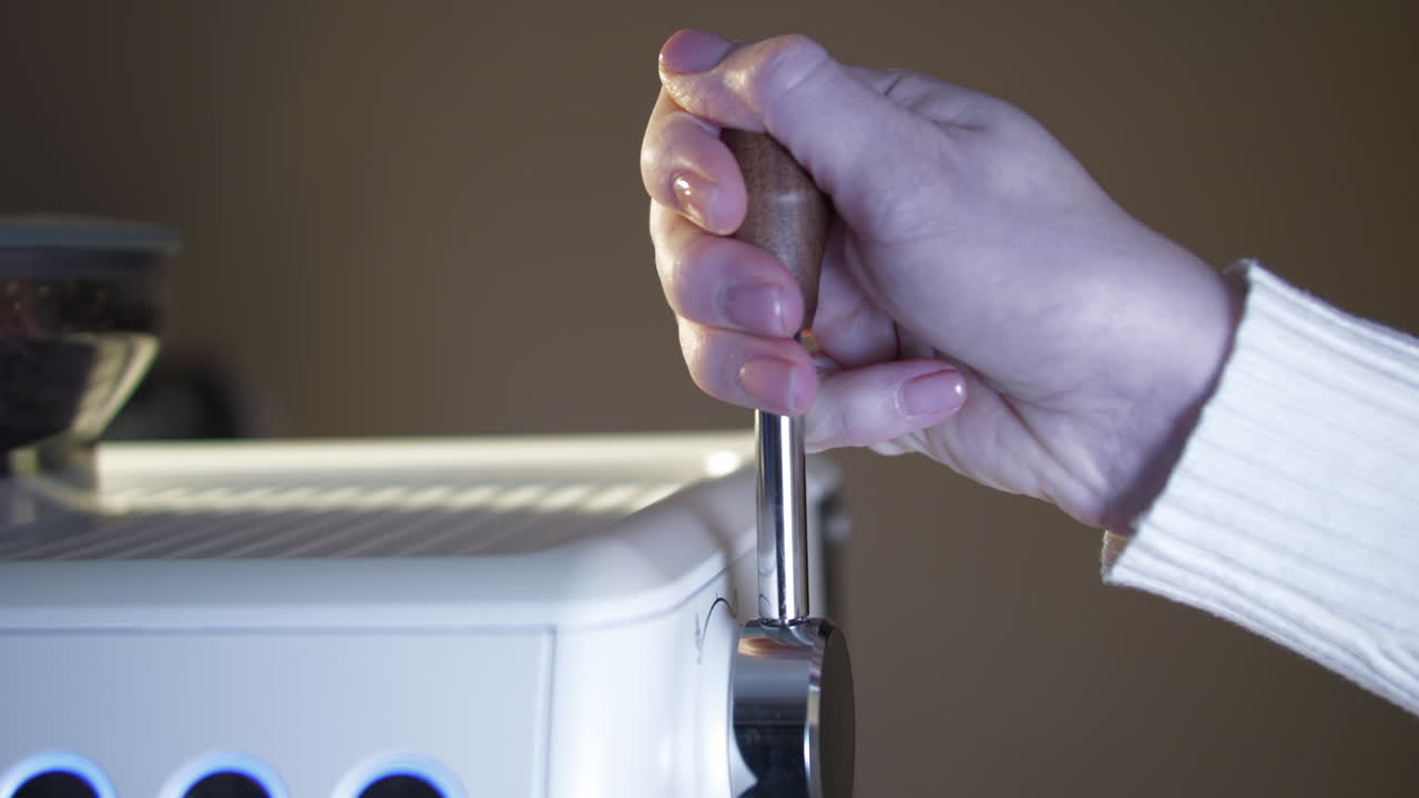 Close up of a female hand pushing back the wooden steam lever on an espresso machine after milk frothing. Warm café lighting highlights tactile control, craftsmanship, and the coffee preparation workf