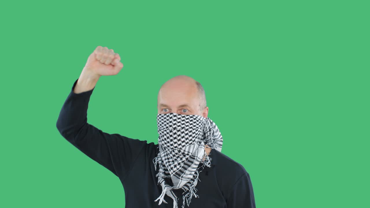Protesterende man met geblokte bandana tijdens demonstratie op groene chromakey-achtergrond. Kale man met gebalde vuist die zingt over sociale revolutie. Volksopstanden en rellen.