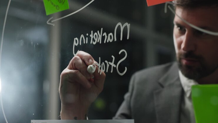 Businessman Writing Marketing Strategy on Glass Board