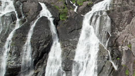 aerial dolly shot pulling back and descending from the top of laukelandsfossen waterfall in norway, revealing multiple gushing streams of water cascading over the rocky cliff face