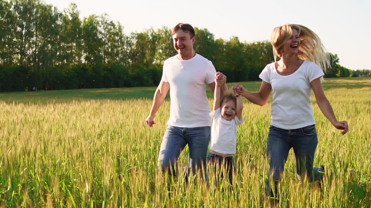 familia feliz: padre, madre e hijo, corriendo en el campo vestidos con camisetas blancas