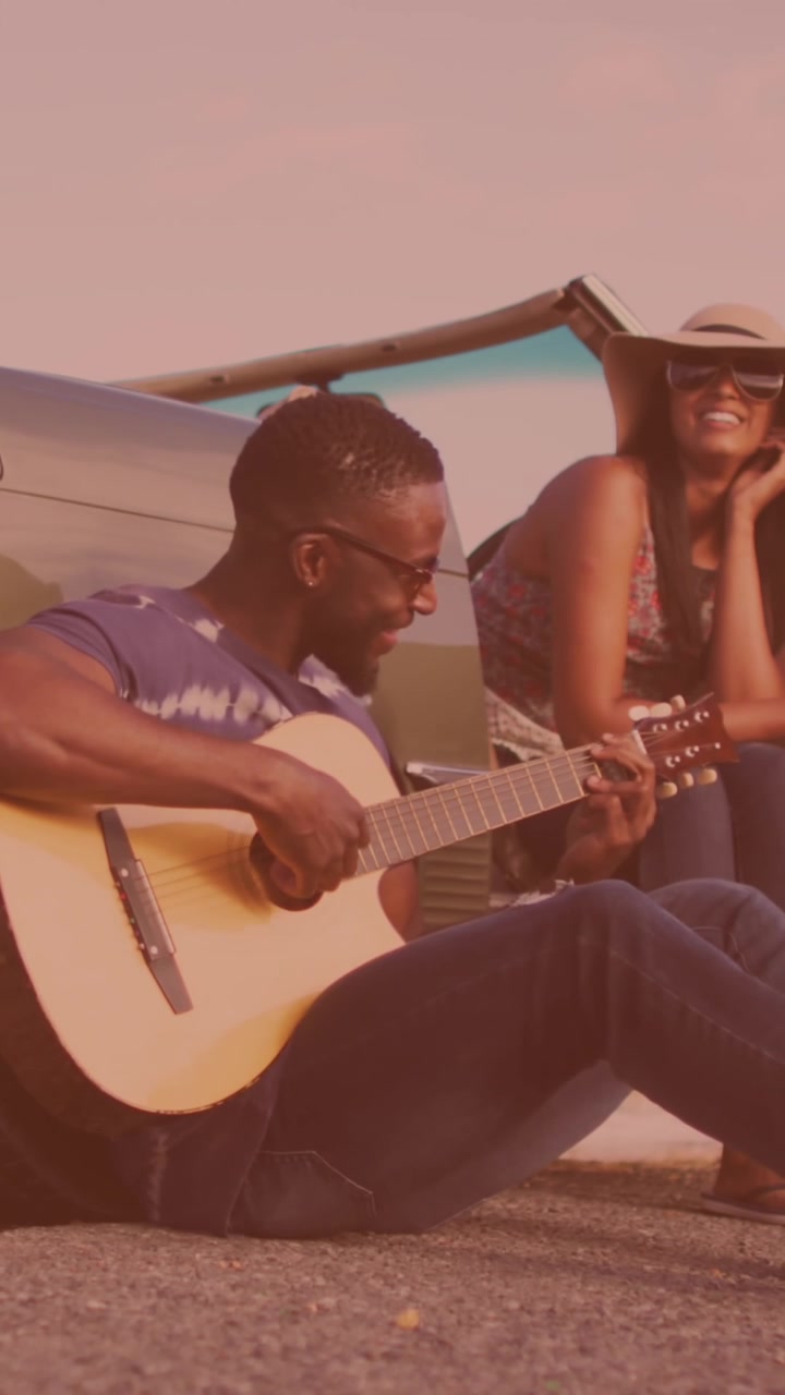 Uomo afroamericano che suona la chitarra per sua moglie vicino all'auto per strada
