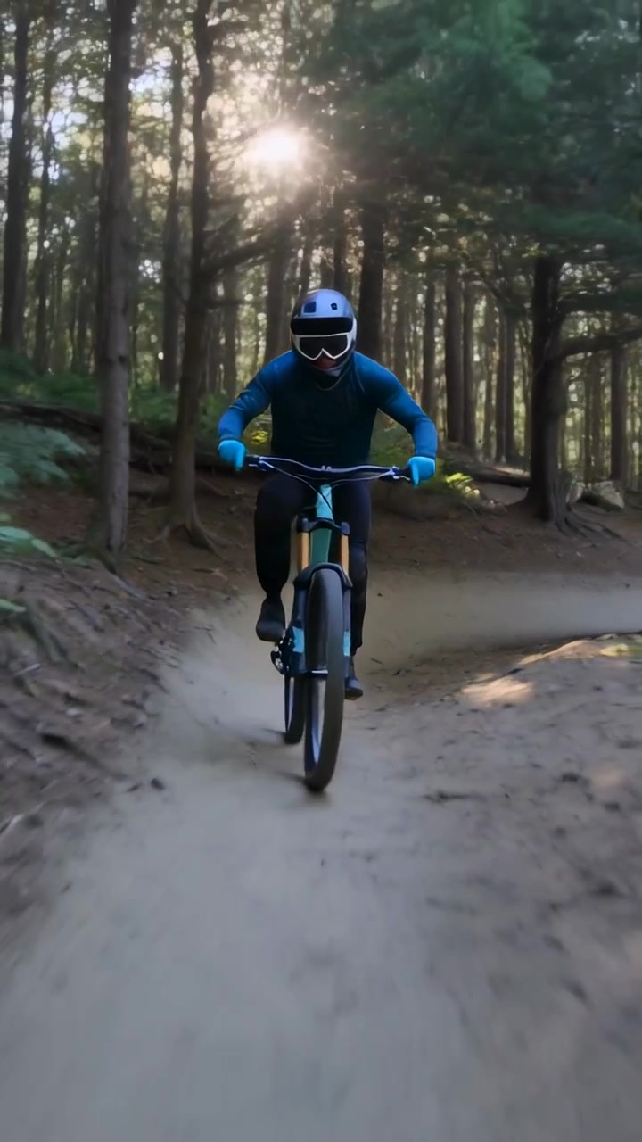 Video verticale: Ciclista con casco che si lancia curvando da una sponda verso l'obiettivo su un sentiero mantenendo la velocità su una MTB verde acqua
