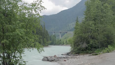 river side view of the majestic park bridge over the light blue rushing water of kicking horse river just below the kicking horse rest area near golden british coumbia, canada