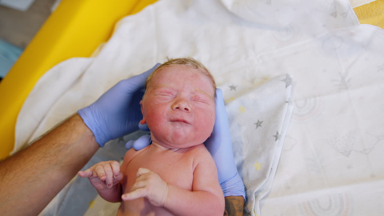 Newborn Caucasian baby lies on the table. Hands of medic in gloves check the baby health and condition. Close up.