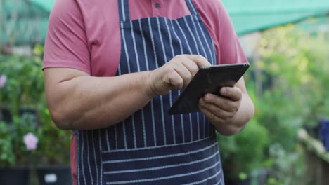 Midsection-of-caucasian-male-gardener-using-tablet-at-garden-center