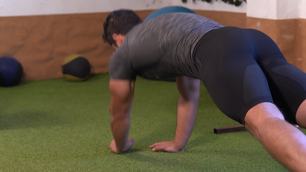 muscular man performing variations of classic plank exercise on gym grass floor