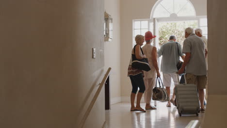 group of senior friends with luggage opening front door and leaving for vacation