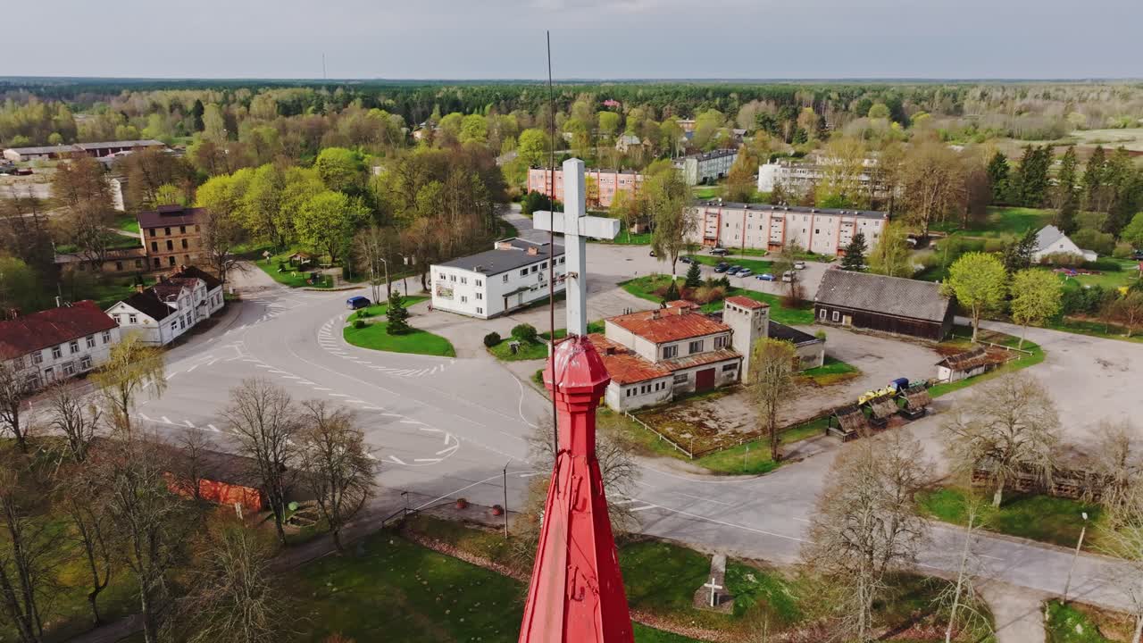 Peaceful aerial rotation reveals church cross rising above Rucava village roofs