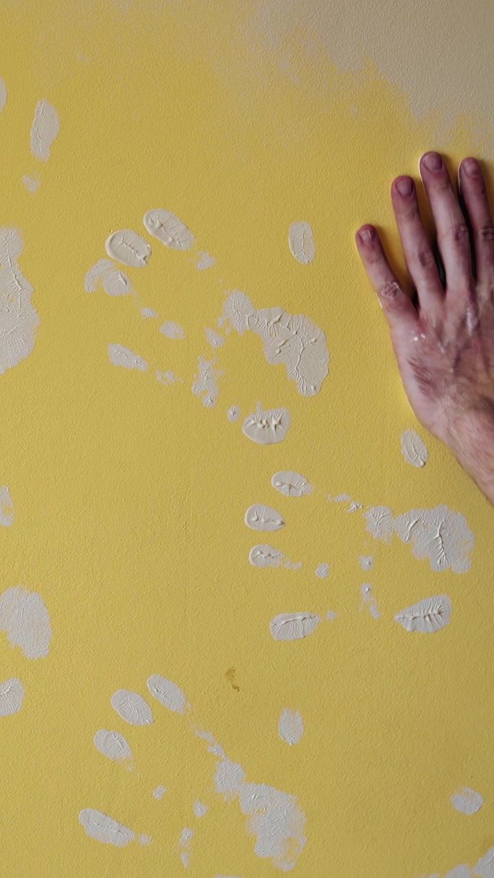 Painter man at work painting an orange wall with a roller. Attractive handsome repairman doing renovation the wall. Vertical video