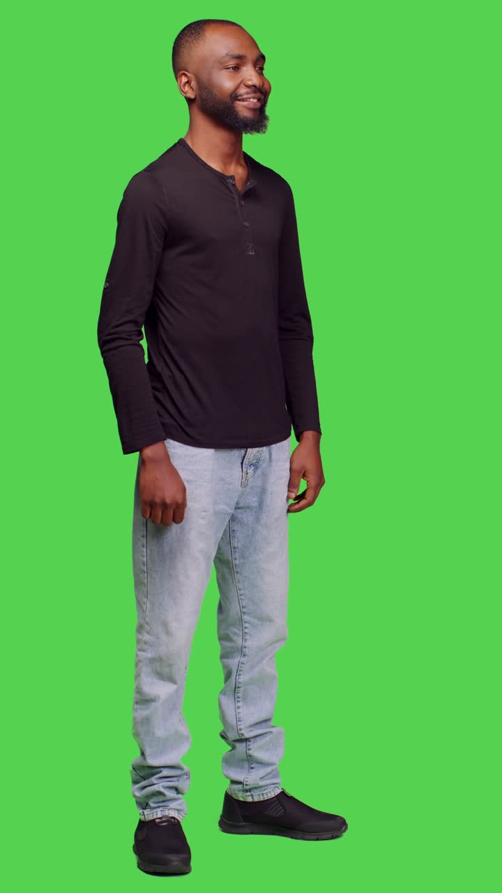 Video verticale: vista laterale di una persona cordiale e casual in posa a figura intera su greenscreen