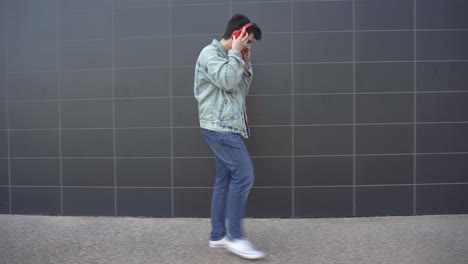 man puts on red headphones connected to a red mobile phone and begins to walk with rhythm and dance down the street