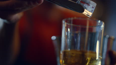 Bar-man-putting-ice-cube-in-glass-inside.-Bartender-mixing-cocktail-on-counter.