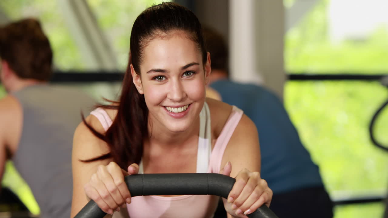 mujer en forma haciendo ejercicio en bicicleta sonriendo a la cámara