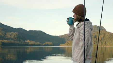 slow motion of young woman drinking morning coffee or tea by the lake in alaska usa, camping concept