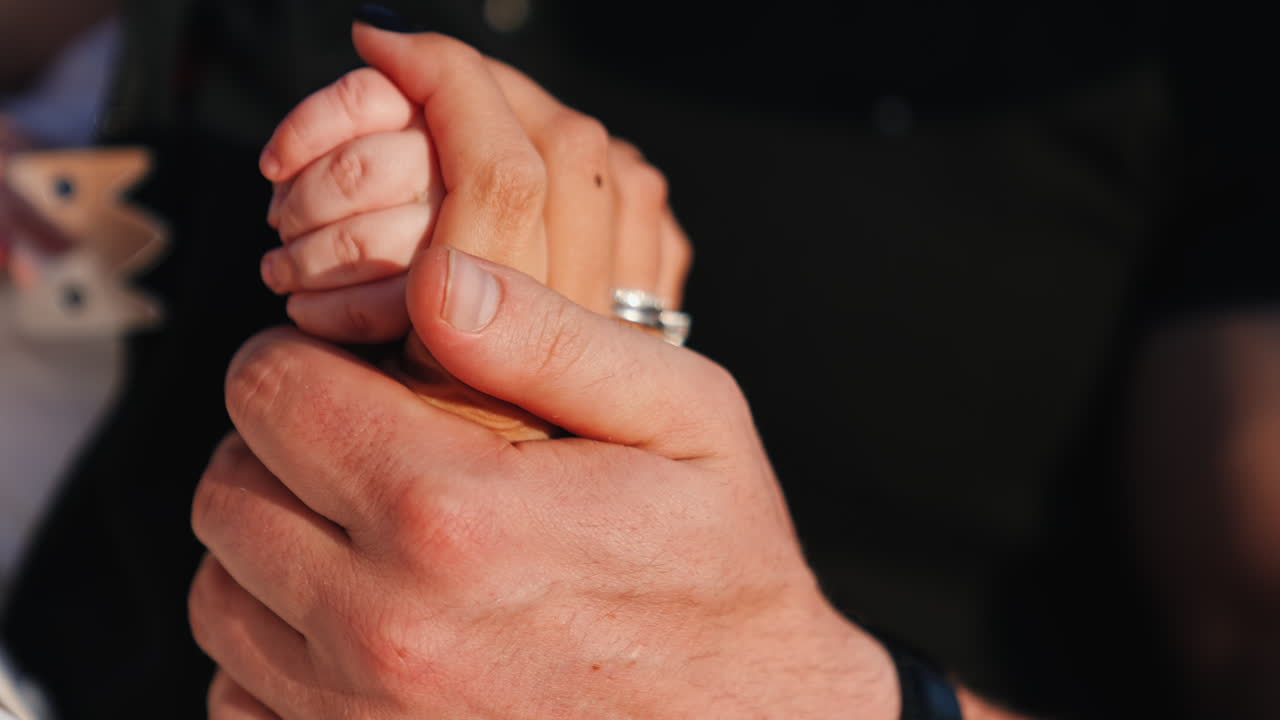 Man stroking a female hand holding a hand of a baby. Family of three close up.