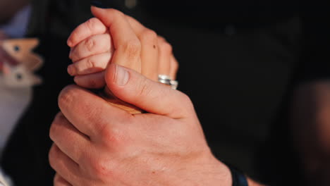 man stroking a female hand holding a hand of a baby. family of three close up.