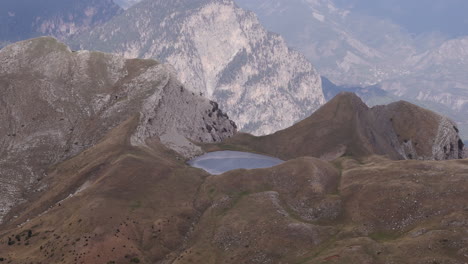 aerial orbit approach to dragonlake on mount tymfi, surrounded by rocky slopes and fog covered peaks
