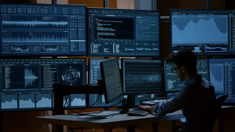 man working at a multi-monitor workstation in a dark control room