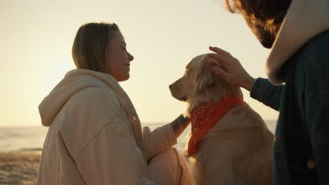 Shooting-up-close:-a-guy-and-a-blonde-girl-are-stroking-a-light-colored-soy-dog-in-the-morning-on-a-sunny-beach.-Beautiful-rays-of-the-sun-in-the-morning